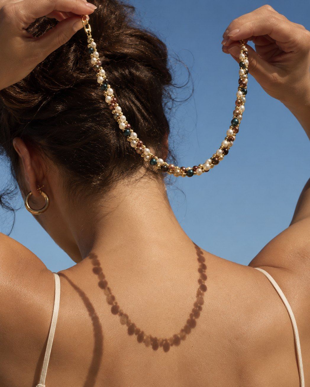 Phaenna necklace held up against a clear blue sky, its shadow falling across a bare back.